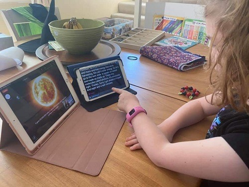 Young girl attending a remote lesson on an iPad using an additional tablet to display the captions from the presentation